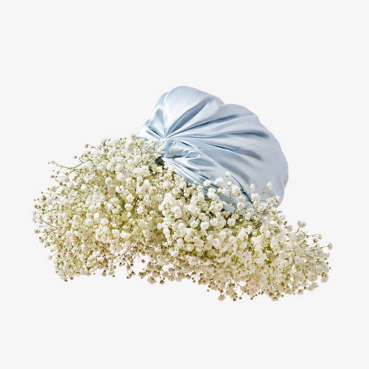 Pale blue silk turban cradling a cloud-like cluster of white baby's-breath flowers on a beige background.