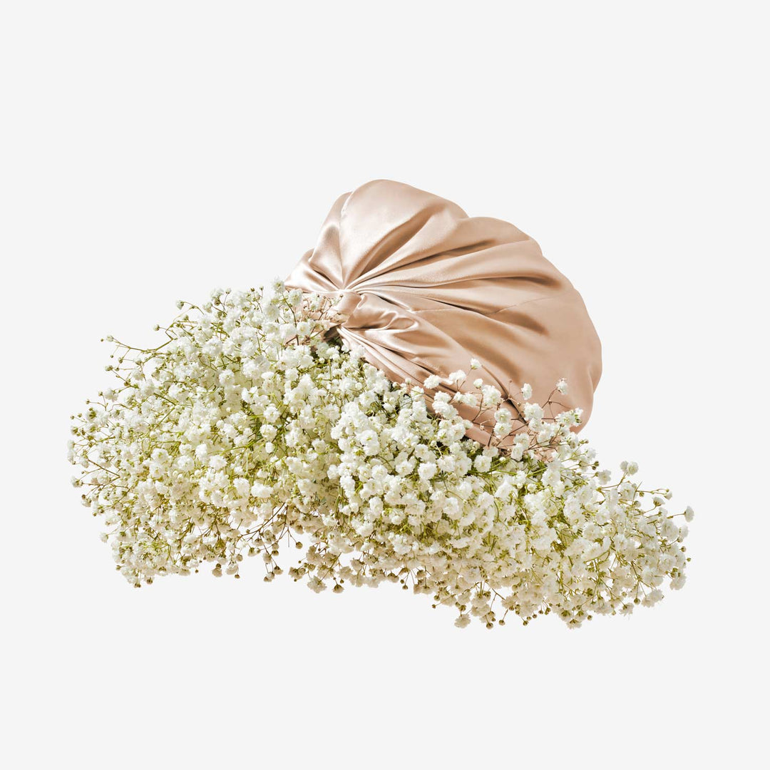 Beige silk turban tied in a knot, adorned with a cloud of white baby's-breath flowers on a pale background