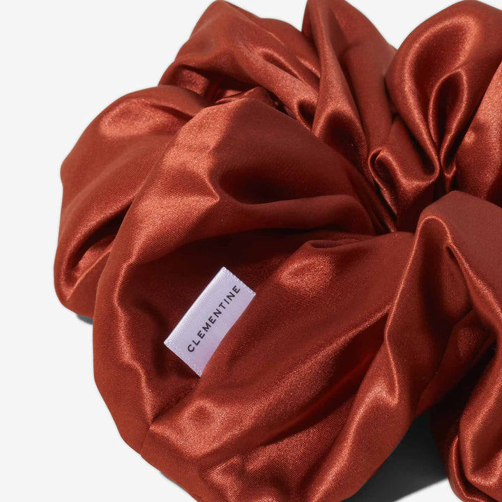 Rust-colored silk scrunchie with white label reading CLEMENTINE