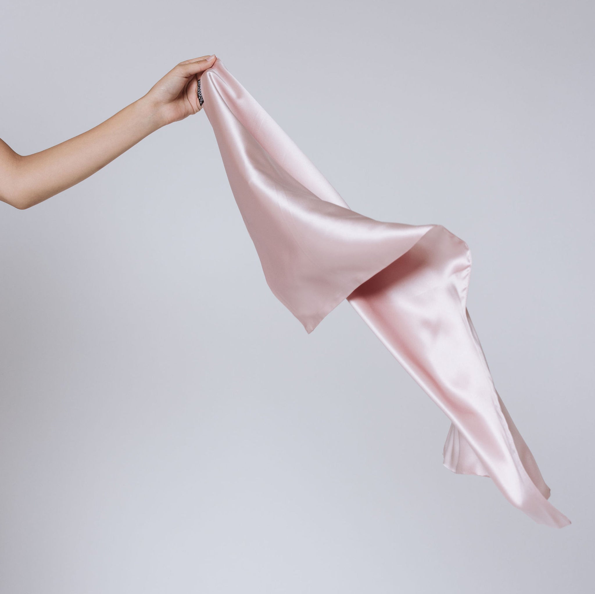 Hand holding a pink silk pillowcase fabric against a plain background