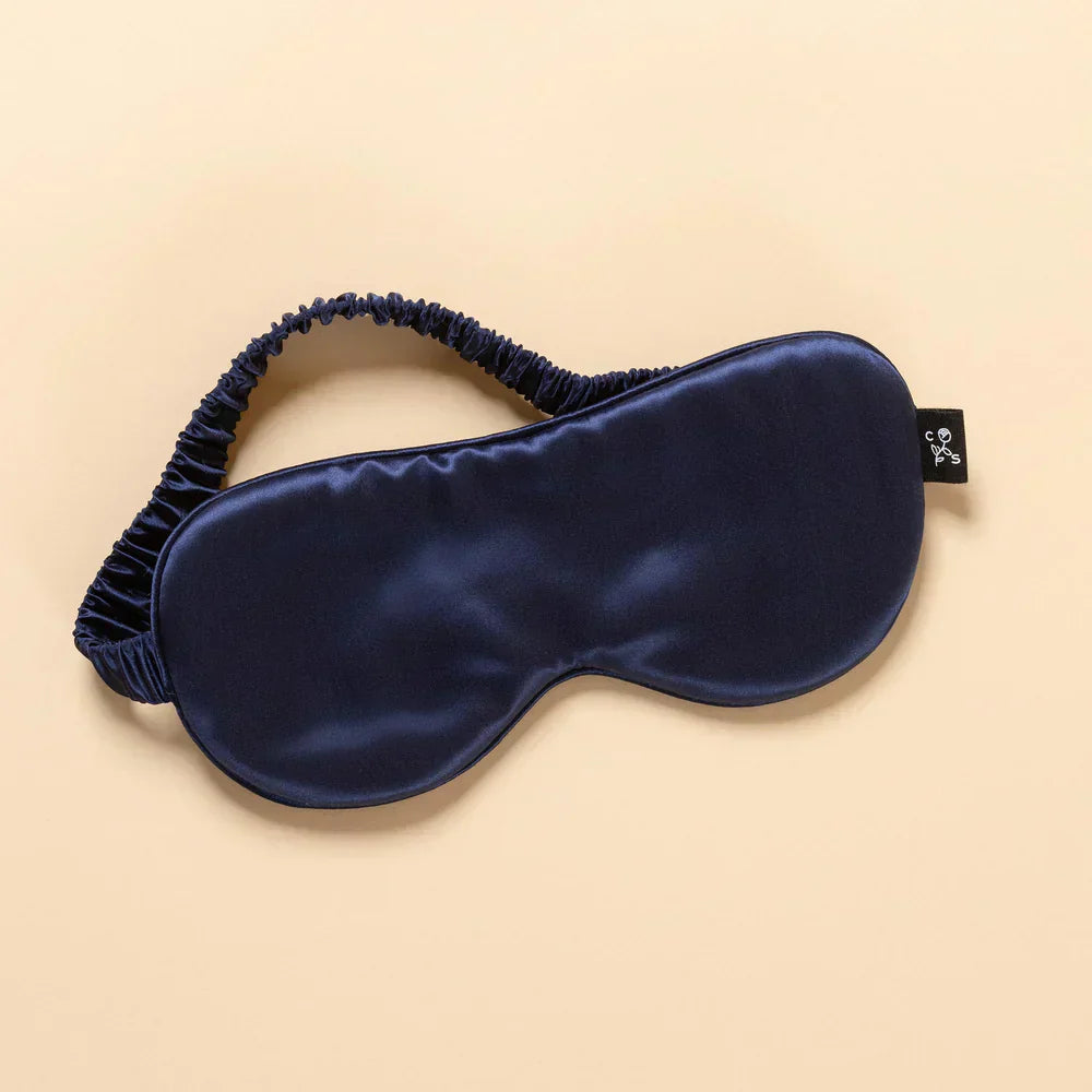 Navy blue silk sleep mask with elastic strap on beige background