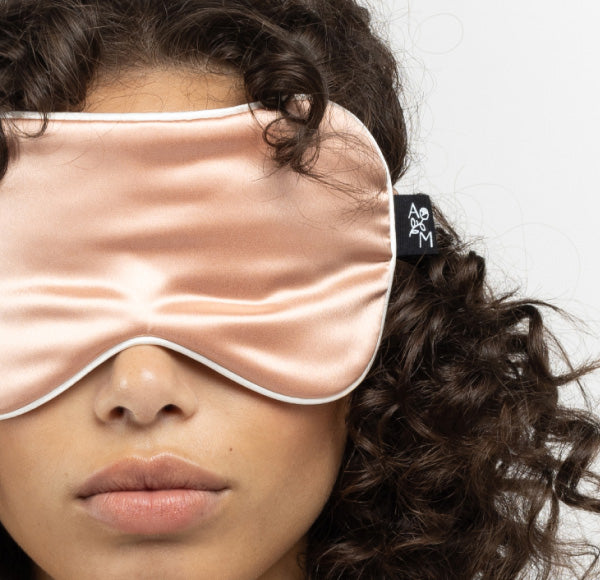Close-up of a person wearing a pink organic silk sleep mask with a black brand tag on the side.