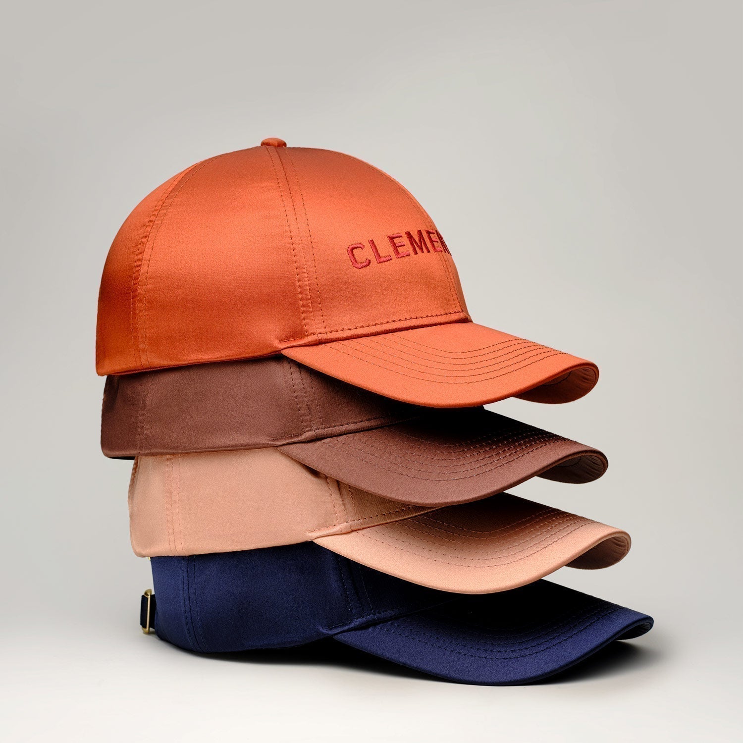 Stack of four caps in orange, brown, peach, and navy, with 