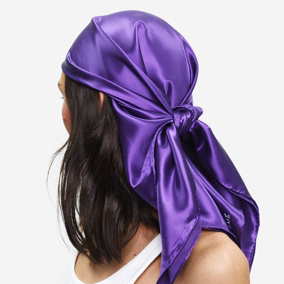Person wearing a purple satin headscarf on a white background. 