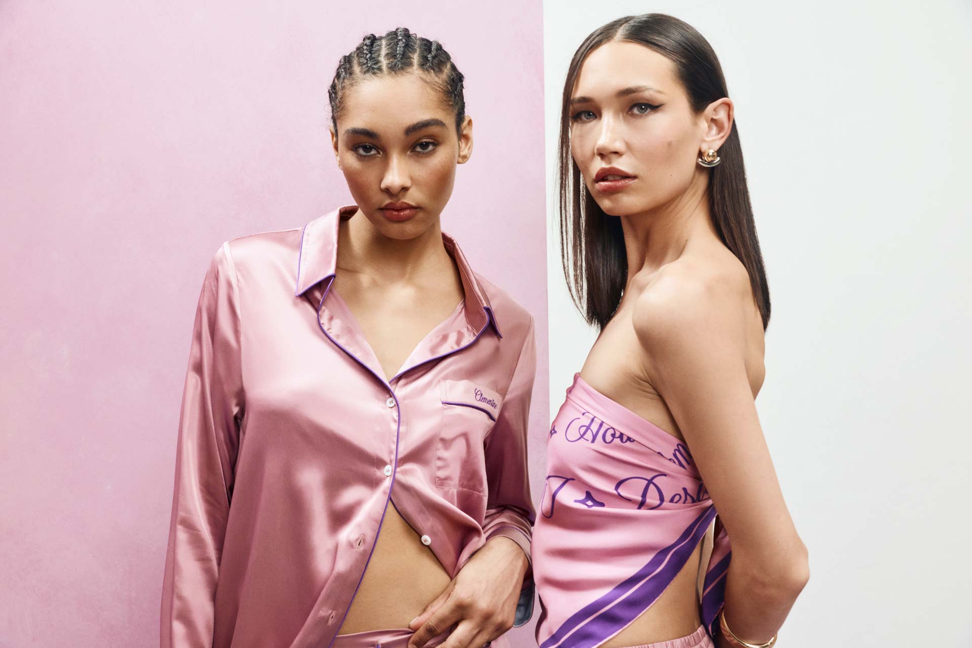 Two models wearing pink silk sleepwear pose against a split pink and white background