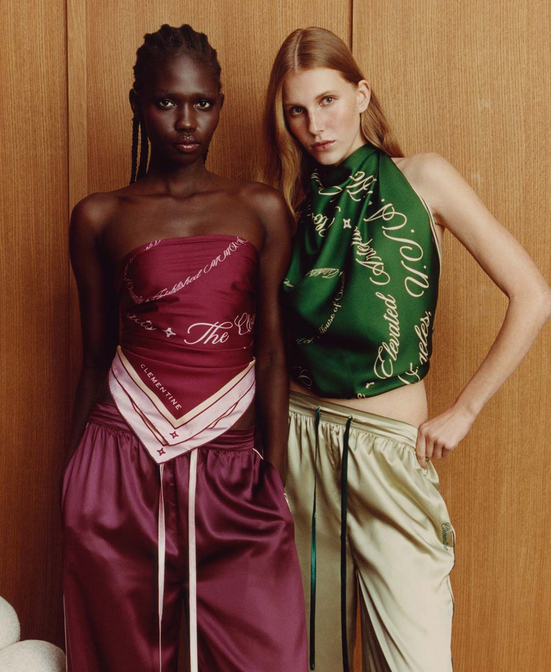 Two models in satin outfits — one in burgundy with CLEMENTINE on a bandana and the script word The; the other in green with a scarf printed Elevated.