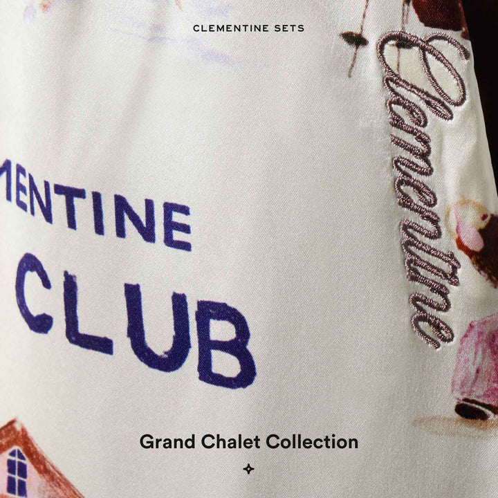 Close-up fabric with printed 'CLEMENTINE SETS CLEMENTINE CLUB', embroidered 'Clementine' and 'Grand Chalet Collection' label.