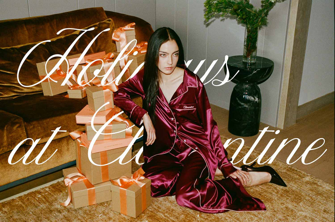 Woman in burgundy silk pajamas beside stacked gift boxes; white script reads 'Holidays at Clementine'.