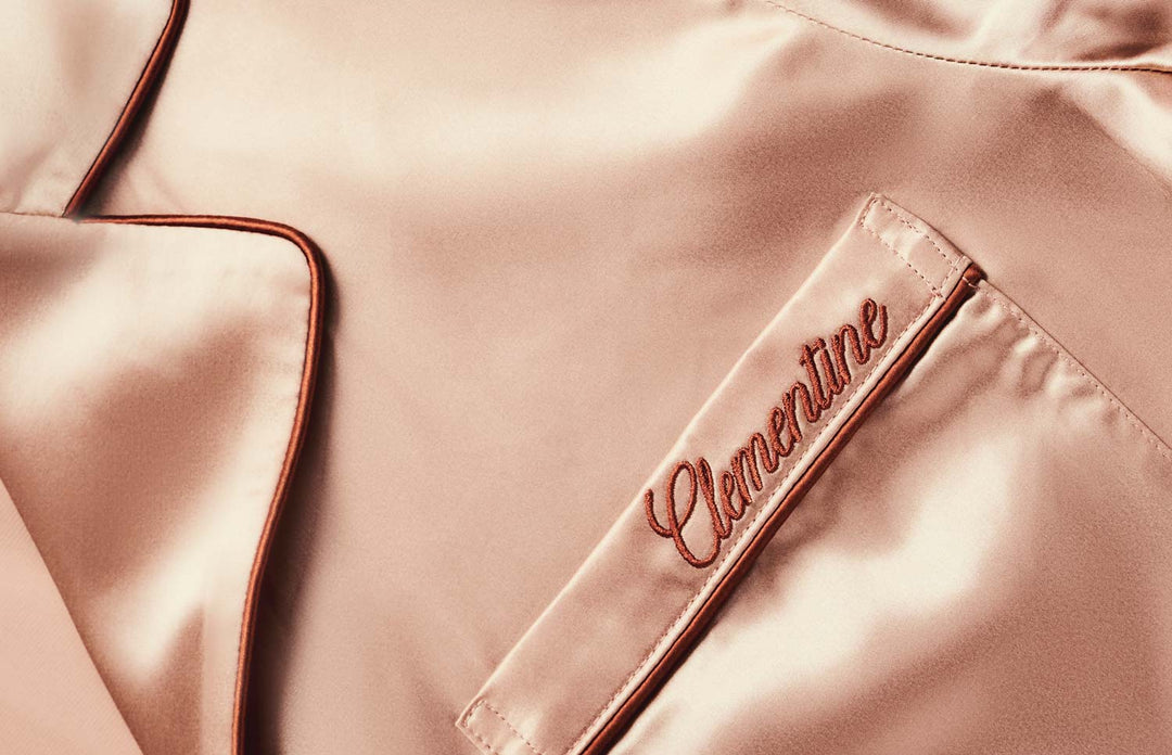 Close-up of silk pajama top showing embroidered ‘Clementine’ name on chest pocket and contrast piping along the collar