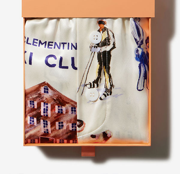 Folded silk scarf in an orange box, illustrated with a skier, chalet and printed text LEMENTIN KI CLU.