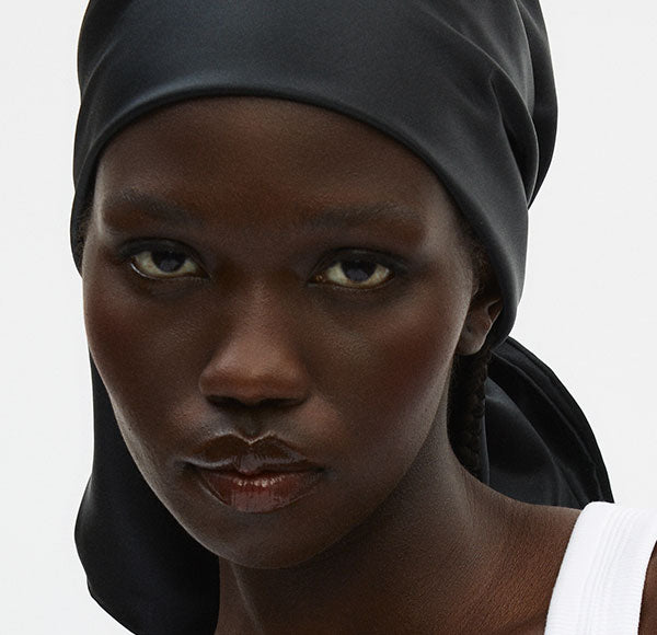 Close-up portrait of a Black woman wearing a black headscarf and white tank top, neutral expression.