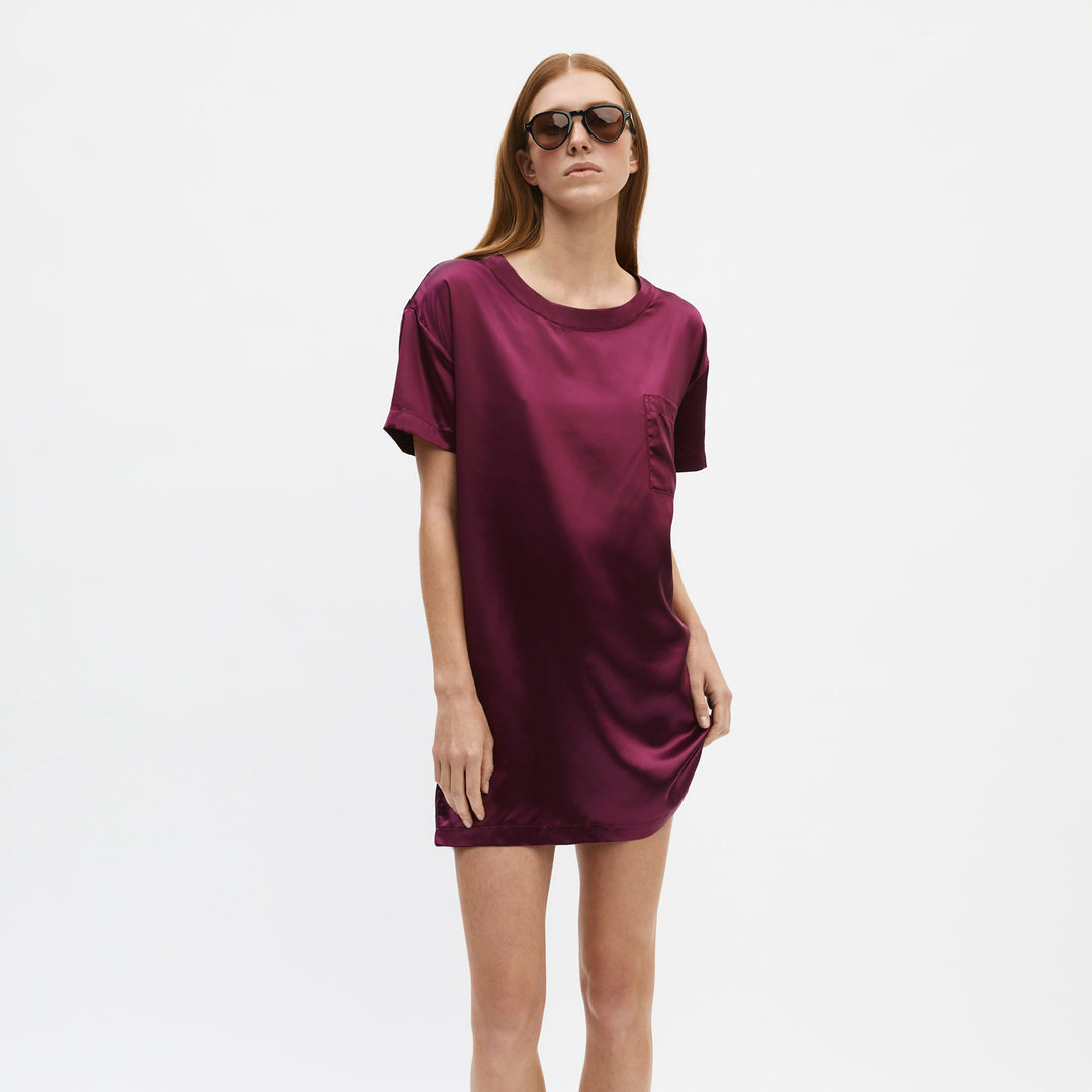 Model wearing short satin burgundy T-shirt dress with chest pocket and sunglasses on white background.