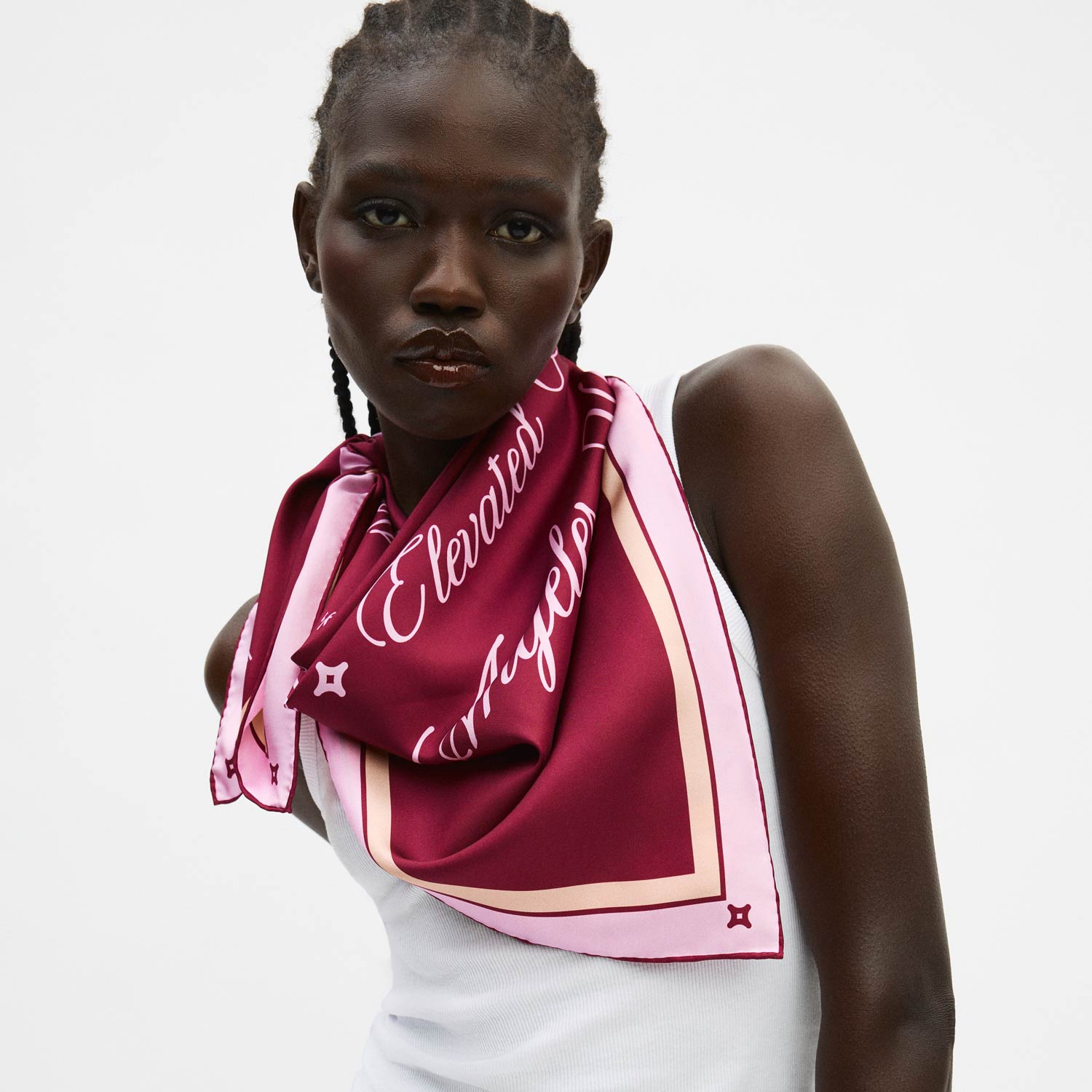 Model wearing mulberry silk scarf tied at shoulder; scarf shows cursive "Elevated" over a white tank top. - #color_mulberry-velvet