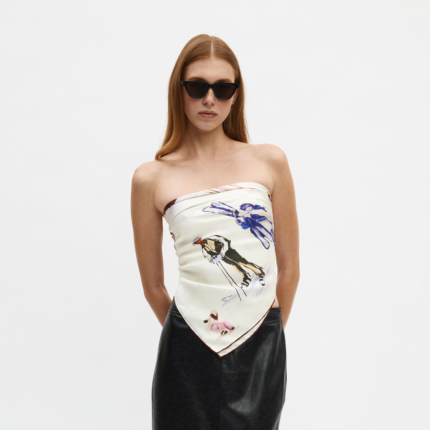 Woman wearing strapless silk scarf top printed with a skier and blue bird, black leather skirt and sunglasses