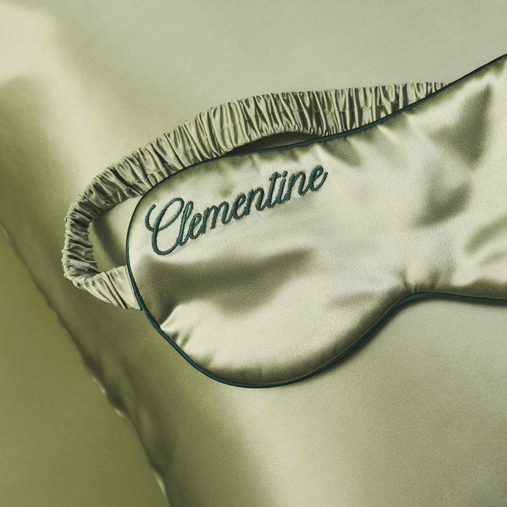Silk sleep mask with 'Clementine' embroidery on a green pillowcase background. #color_kyoto