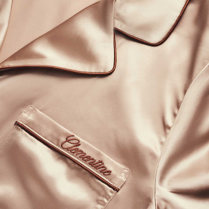 Close-up of a peach silk garment with 'Clementine' branding embroidered on pocket.#color_clementine-peach-and-dusk